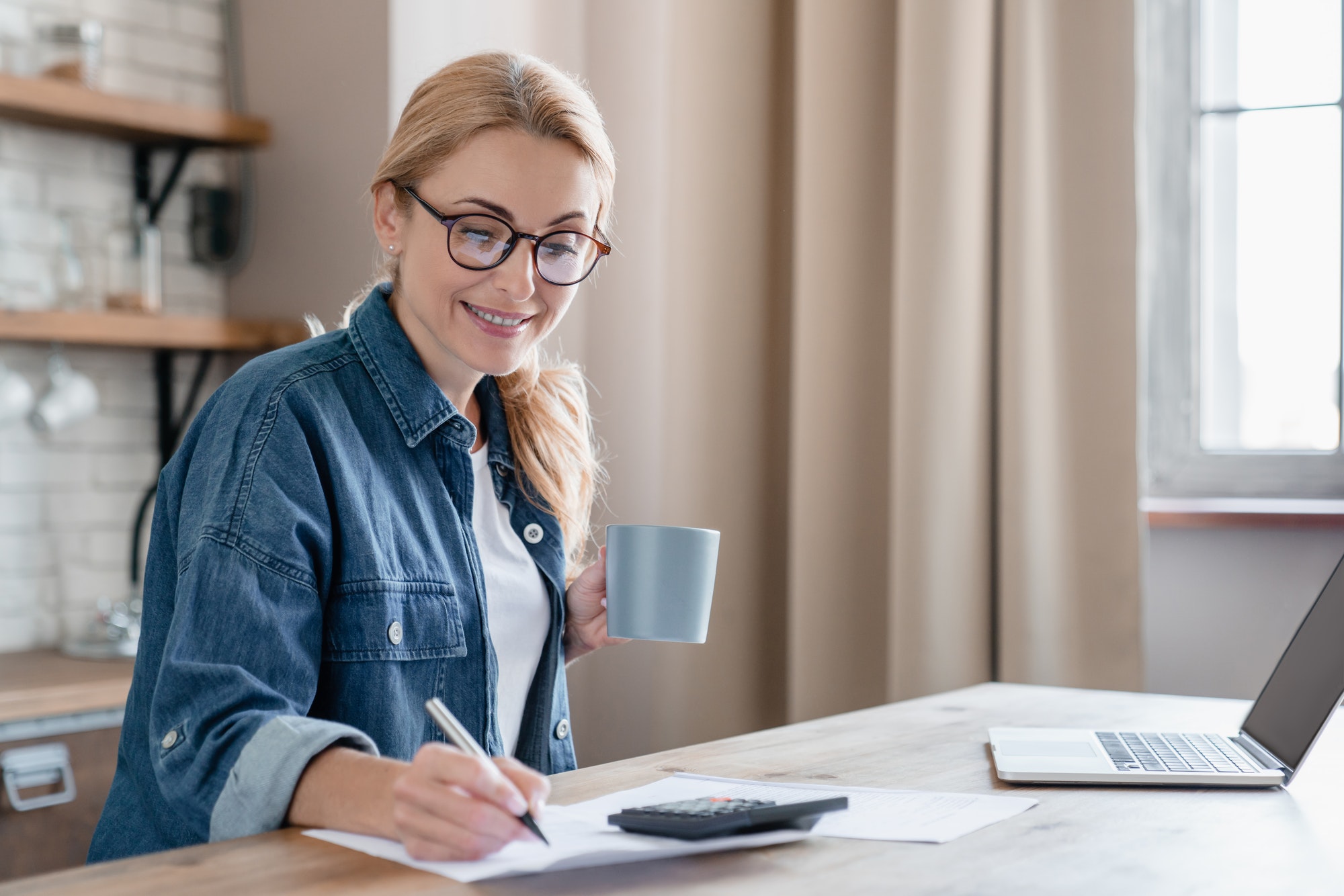 Happy smart mature woman financial advisor taking notes, concentrated on home bills calculations